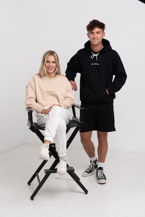 Fashion Photographer North Shore Blond Woman wearing a cream outfit sitting of a black chair with a man standing